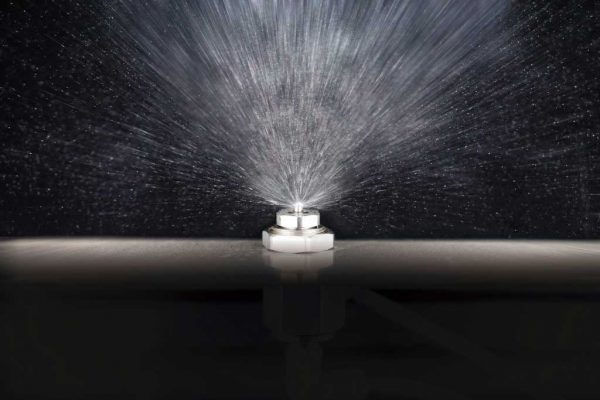 アンベル洗浄段階①吹き付ける　「アンベル専用に開発したアルコール洗浄剤（ベルウォッシュ）を特殊な噴霧ノズルでベルト面に吹きつけ、短時間で安定的に洗浄します。スクレイパーがベルト面に付着した異物や生菌の除去作業の効果も向上させます。」